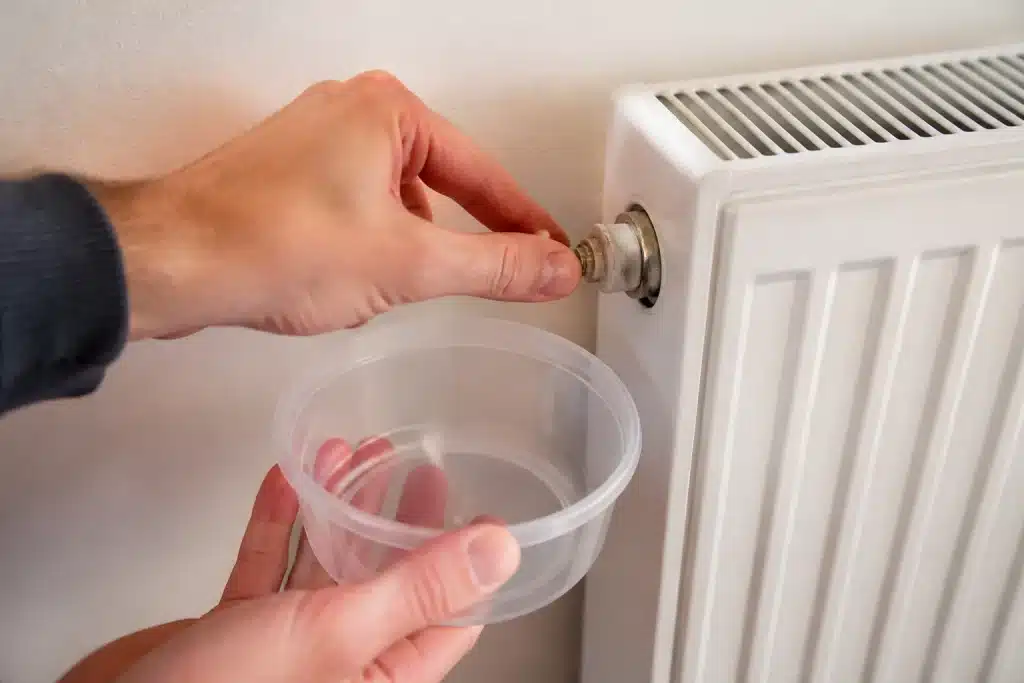 Main tenant cle purge radiateur avec recipient eau