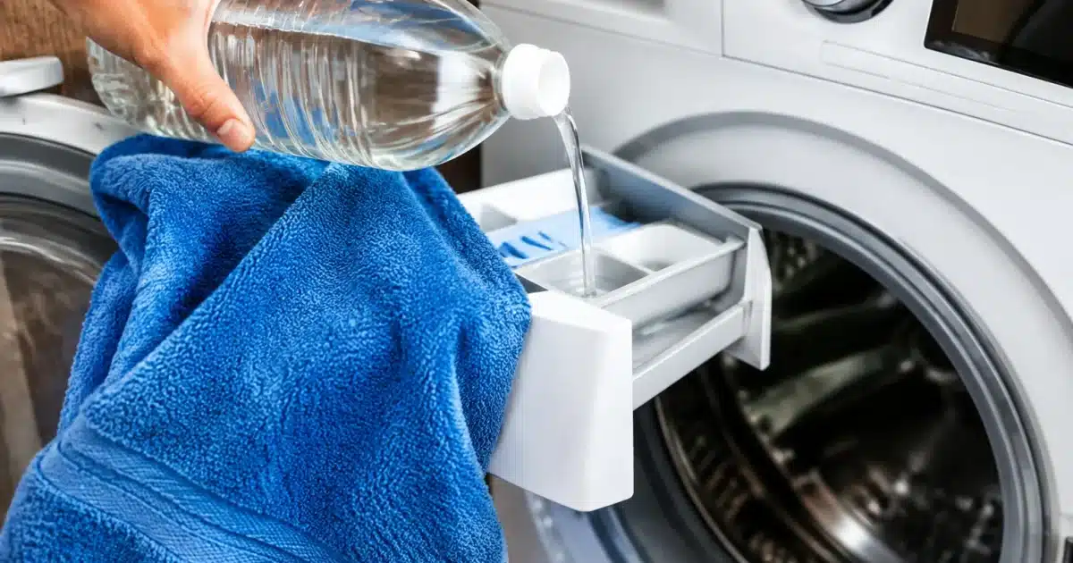Serviette éponge posée sur lave-linge ouvert avec vinaigre blanc versé dans bac adoucissant