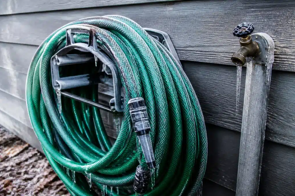 Tuyau d'arrosage enroule pres d'un robinet exterieur gele