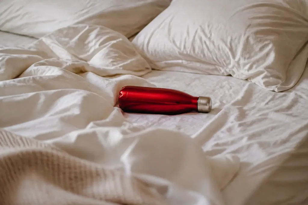 Bouteille rouge posee sur un lit defait