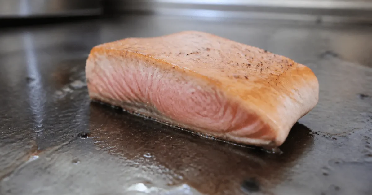 Filet de saumon rose saignant sur plaque chauffante metallique.