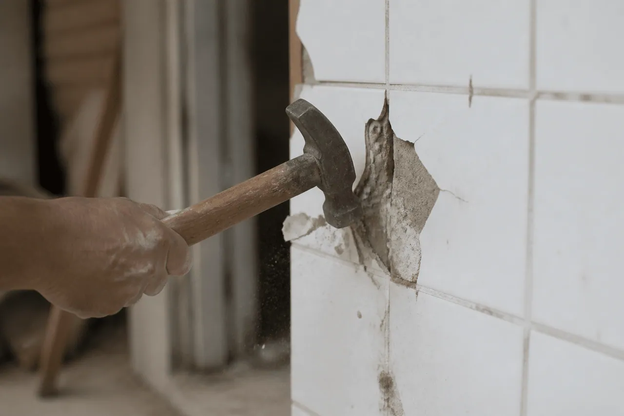Marteau frappant un carreau de mur blanc endommagé.
