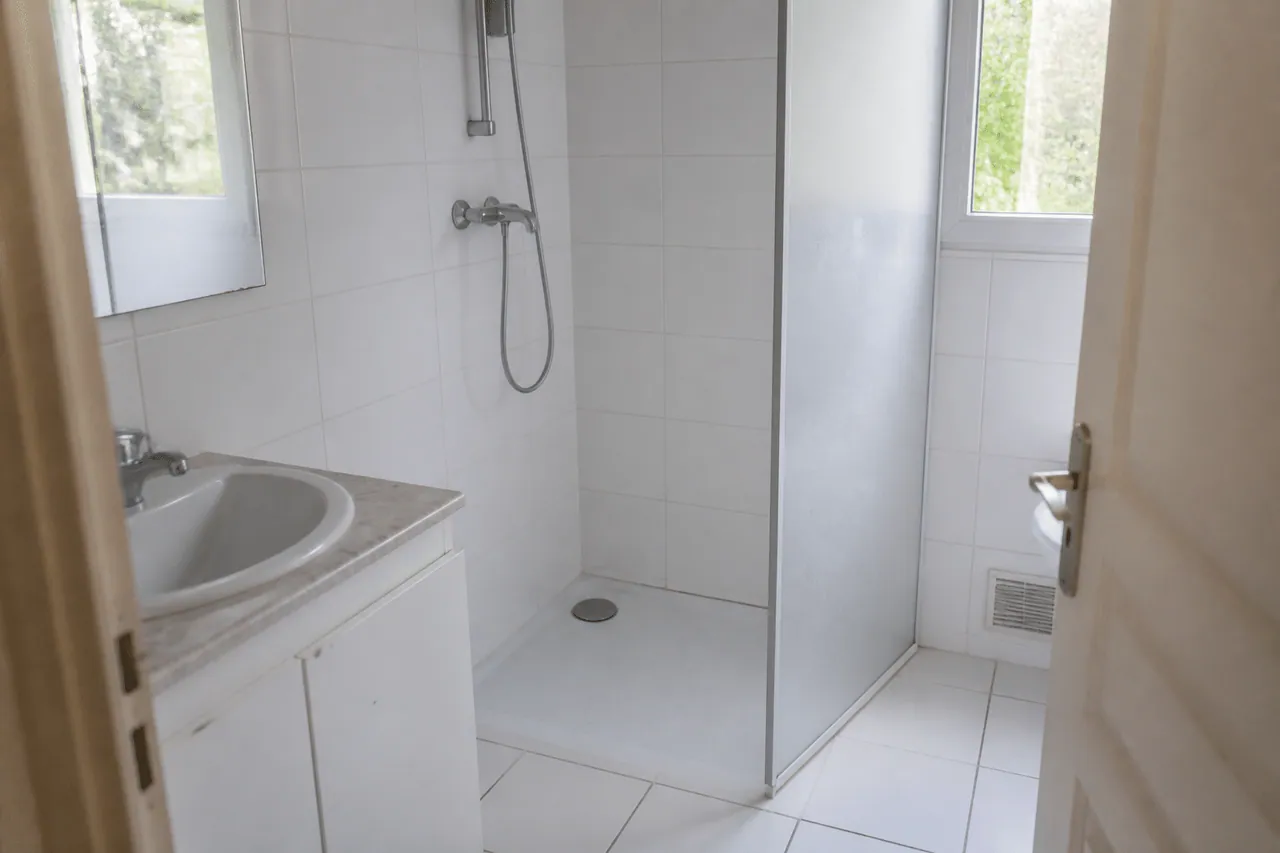 Salle de bain blanche carrelage ceramique, douche PVC, vasque simple.