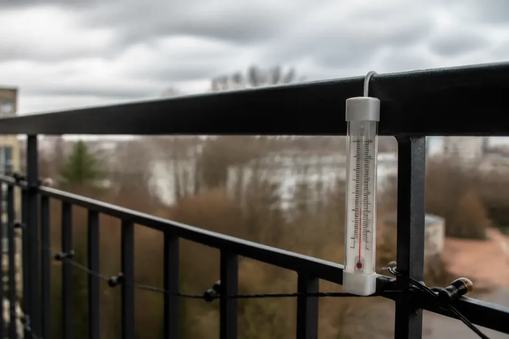 Thermometre exterieur accroche a un balcon sous ciel gris